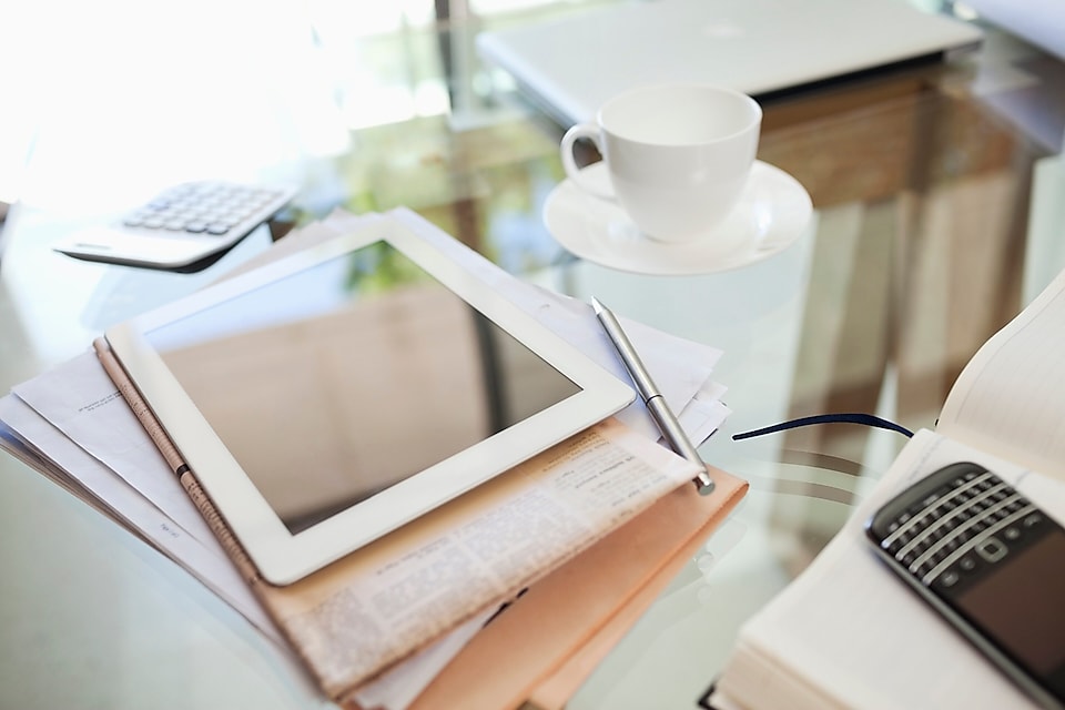 Tablet computer, newspaper, coffee cup and cell phone on desk